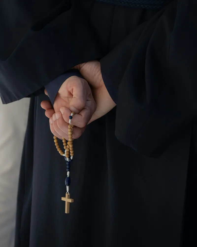 Mãos segurando um terço de madeira